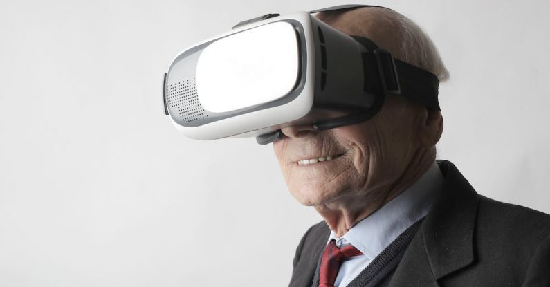 VR Innovation - Smiling elderly gentleman wearing classy suit experiencing virtual reality while using modern headset on white background