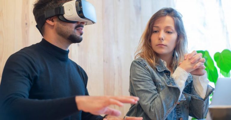 VR Meeting - A Woman Sitting Besides a Man Wearing VR Goggles