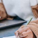 Remote Work City - Unrecognizable female student taking notes while preparing for exam using netbook on street