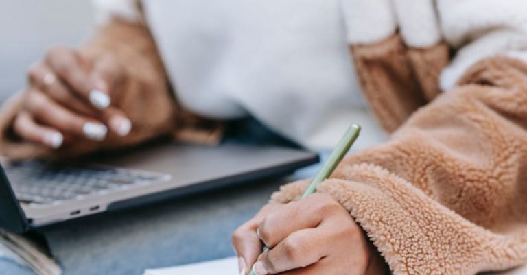 Remote Work City - Unrecognizable female student taking notes while preparing for exam using netbook on street