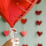 Four-day Workweek - A person holding a red heart shaped balloon in front of a wall of hearts