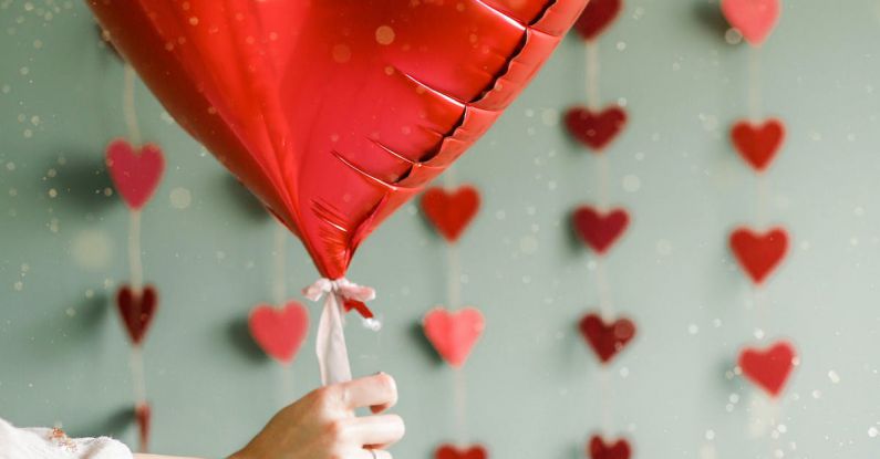 Four-day Workweek - A person holding a red heart shaped balloon in front of a wall of hearts