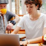 Remote Team Global - Pensive young woman typing on netbook while man with cup drinking coffee at table of cafe