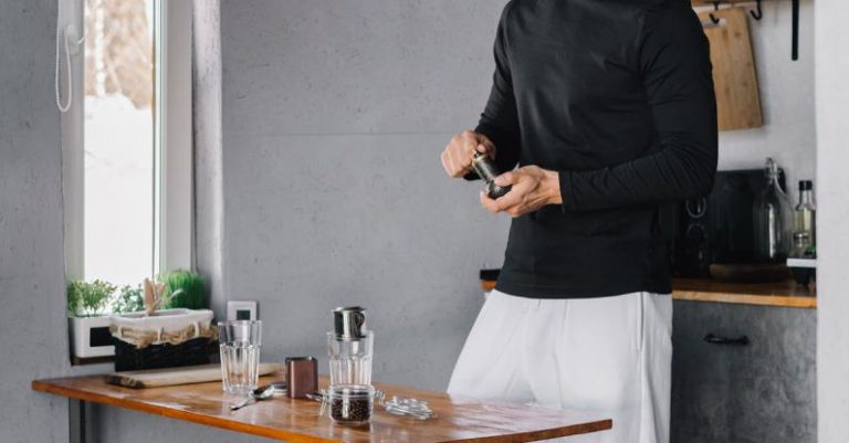 Employee Mental Health - Man in Black Long Sleeve Shirt and White Pants Standing Beside Brown Wooden Table