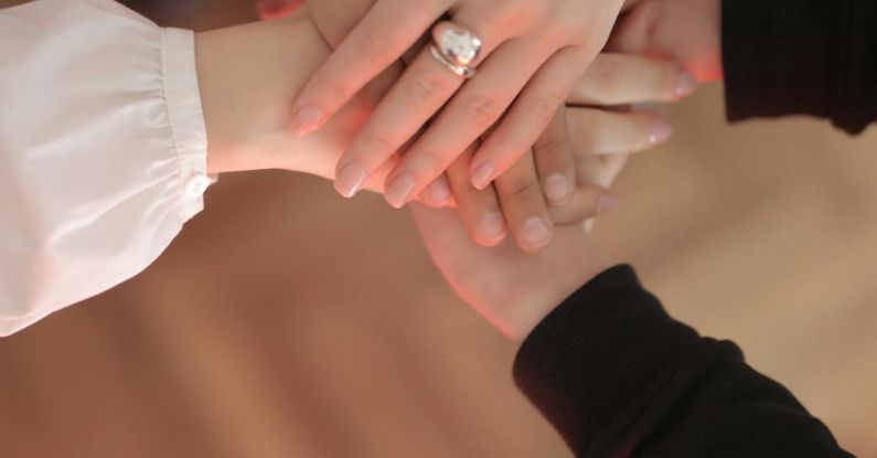 Community Meeting - Top view of faceless friends in different clothes stacking hands together while standing on wooden floor indoor on sunny day