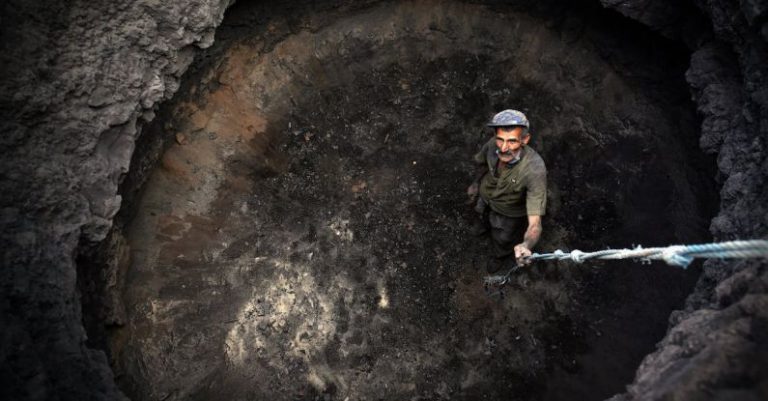 Asteroid Mining - Man in Green Shirt and Black Pants Holding Black and White Stick in Brown Cave