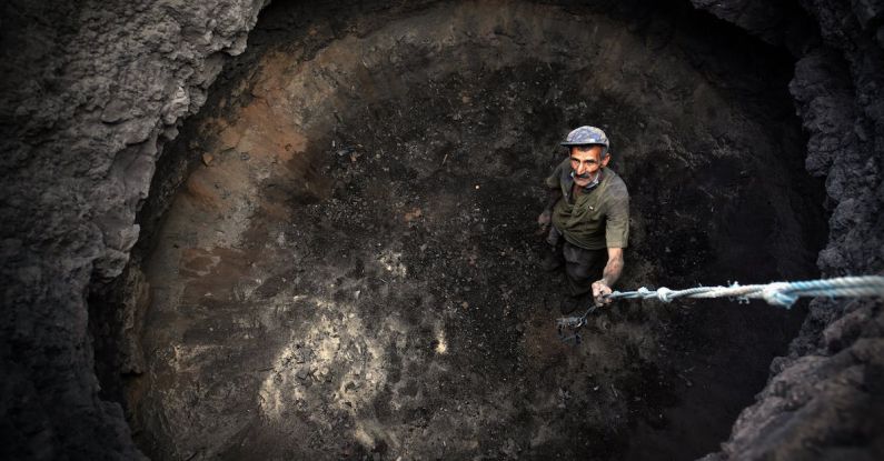 Asteroid Mining - Man in Green Shirt and Black Pants Holding Black and White Stick in Brown Cave