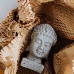 Online Safety Gaming - Top view of gray stone bust of Buddha placed on white marble table in cardboard box with craft perforated paper after receiving postal delivery