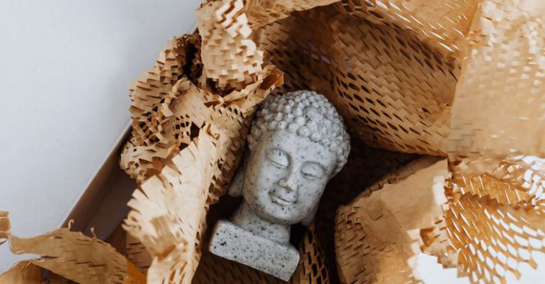 Online Safety Gaming - Top view of gray stone bust of Buddha placed on white marble table in cardboard box with craft perforated paper after receiving postal delivery